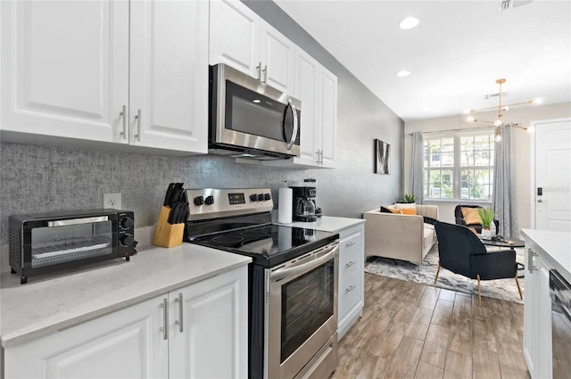 kitchen with decorative backsplash, appliances with stainless steel finishes, light wood-type flooring, and white cabinetry