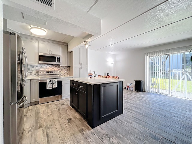 kitchen with light hardwood / wood-style flooring, a textured ceiling, tasteful backsplash, a kitchen island, and stainless steel appliances