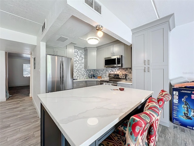 kitchen with a kitchen bar, light stone countertops, light wood-type flooring, and appliances with stainless steel finishes