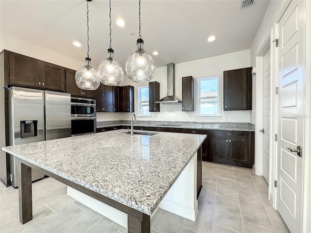 kitchen with stainless steel appliances, a kitchen island with sink, sink, wall chimney range hood, and hanging light fixtures