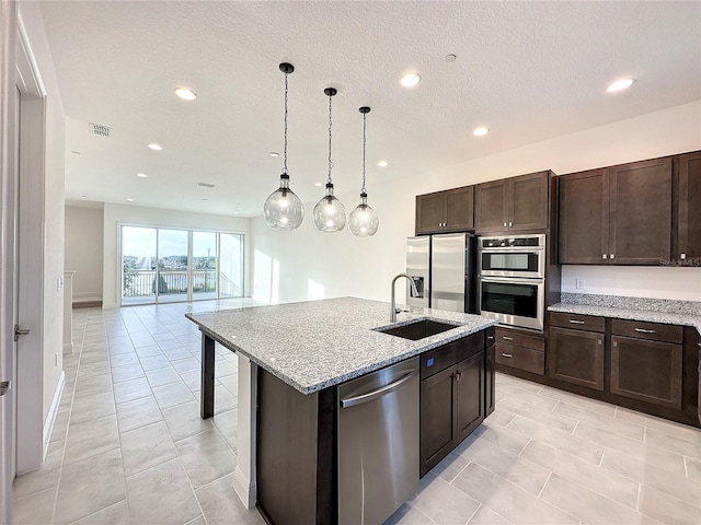 kitchen with light stone countertops, sink, decorative light fixtures, a center island with sink, and appliances with stainless steel finishes