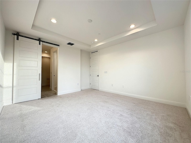 unfurnished bedroom featuring a barn door, a raised ceiling, and light colored carpet