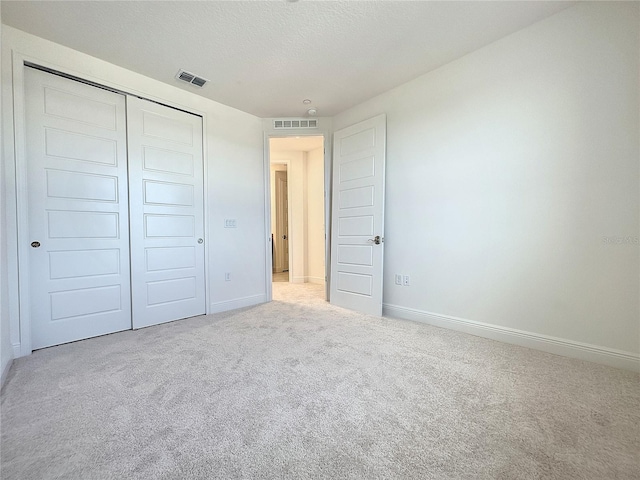 unfurnished bedroom featuring light carpet, a textured ceiling, and a closet