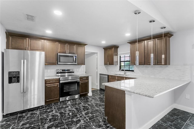 kitchen with appliances with stainless steel finishes, pendant lighting, tasteful backsplash, light stone counters, and kitchen peninsula