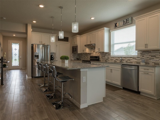 kitchen featuring light stone countertops, a center island, stainless steel appliances, and dark wood-type flooring