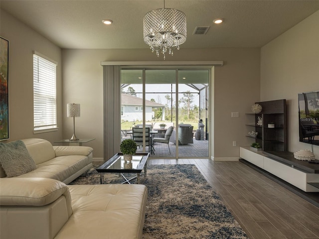 living room with a healthy amount of sunlight, wood-type flooring, a textured ceiling, and an inviting chandelier