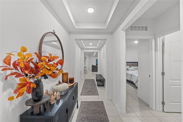 hallway featuring a tray ceiling and light tile patterned flooring