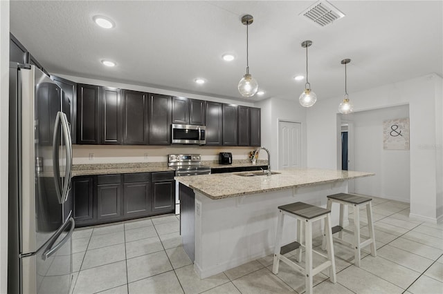 kitchen featuring a center island with sink, sink, hanging light fixtures, light stone countertops, and appliances with stainless steel finishes