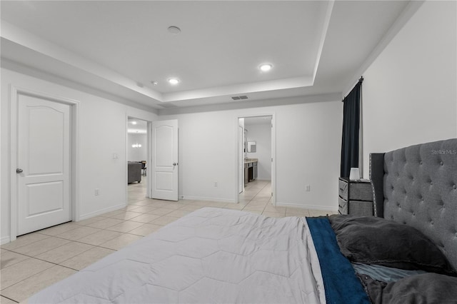 bedroom with ensuite bathroom, light tile patterned floors, and a tray ceiling