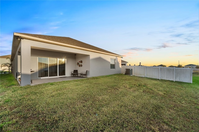 back house at dusk with central AC, a patio area, and a lawn