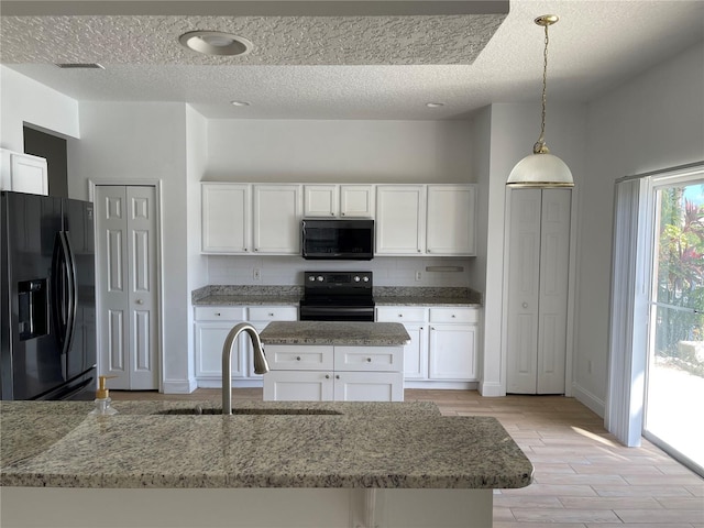 kitchen featuring light wood-type flooring, black appliances, a sink, white cabinets, and light stone countertops