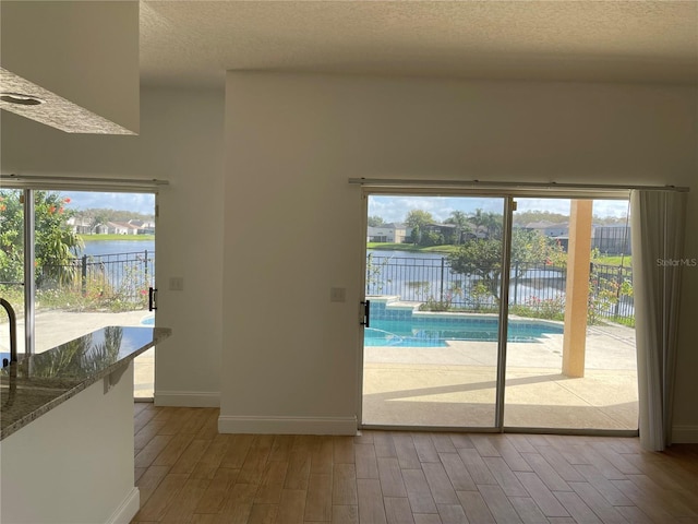 doorway with a textured ceiling, wood finished floors, baseboards, and a water view