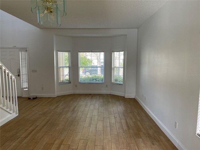 unfurnished living room featuring light wood finished floors, a chandelier, a textured ceiling, and baseboards