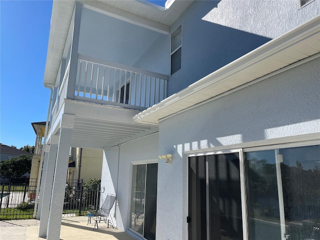 exterior space featuring stucco siding, a balcony, and fence