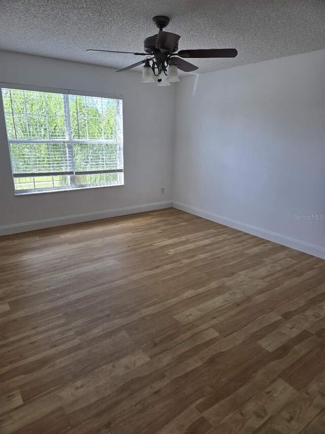 spare room with a ceiling fan, wood finished floors, baseboards, and a textured ceiling