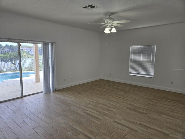 spare room featuring visible vents, a ceiling fan, a textured ceiling, wood finished floors, and baseboards