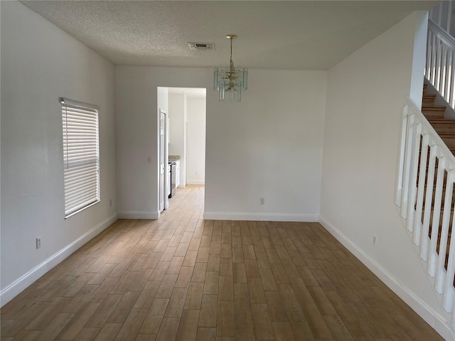 unfurnished room featuring stairway, wood finished floors, visible vents, a textured ceiling, and a notable chandelier