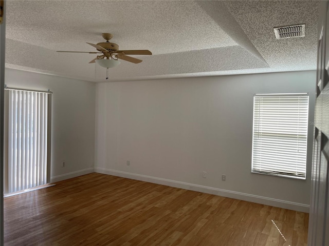 empty room with visible vents, a textured ceiling, wood finished floors, and a ceiling fan