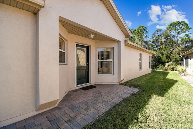 view of exterior entry with a lawn and a patio