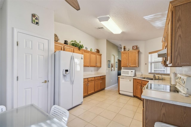 kitchen with white appliances, sink, vaulted ceiling, light tile patterned floors, and a textured ceiling