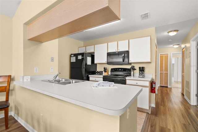 kitchen featuring kitchen peninsula, light wood-type flooring, white cabinetry, and black appliances