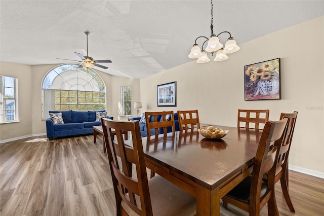 dining area with light wood finished floors, baseboards, ceiling fan, vaulted ceiling, and a textured ceiling