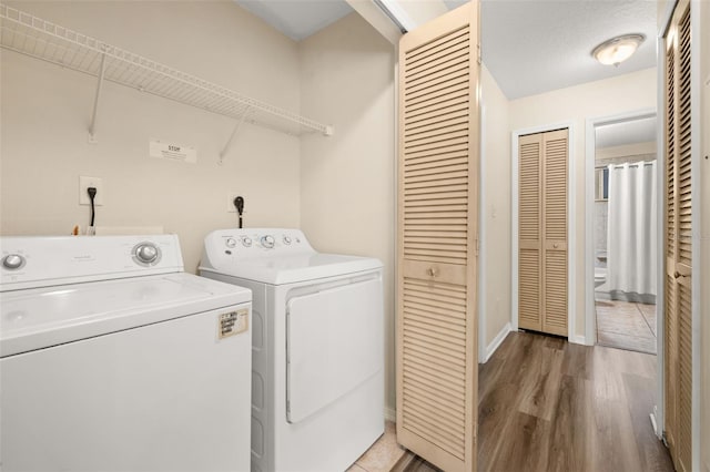 washroom featuring laundry area, baseboards, separate washer and dryer, and wood finished floors