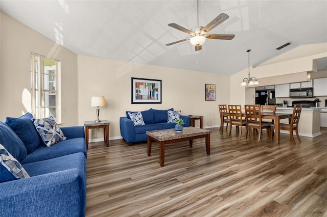 living area featuring vaulted ceiling, ceiling fan with notable chandelier, baseboards, and light wood-style floors