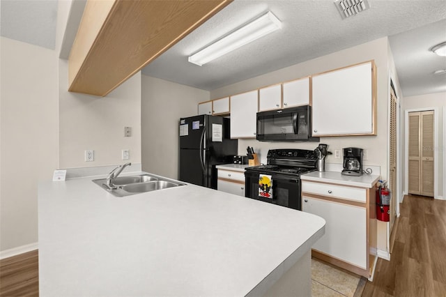 kitchen featuring white cabinets, a peninsula, light countertops, black appliances, and a sink