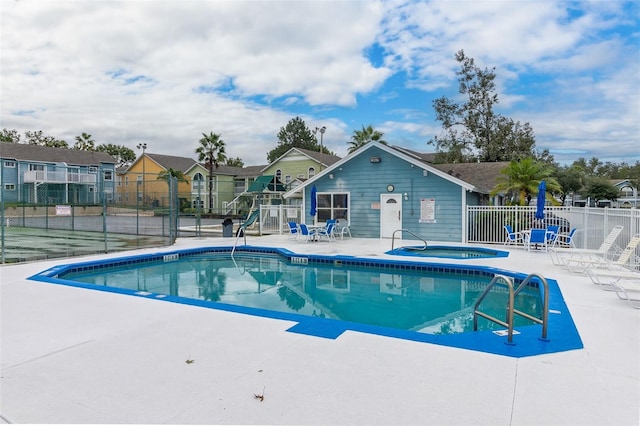 view of swimming pool with a community hot tub, playground community, a patio area, fence, and a residential view