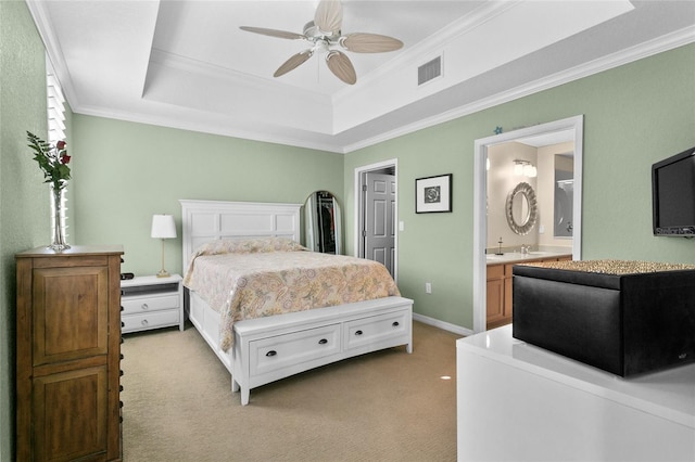 carpeted bedroom featuring a raised ceiling, ensuite bath, ceiling fan, and crown molding