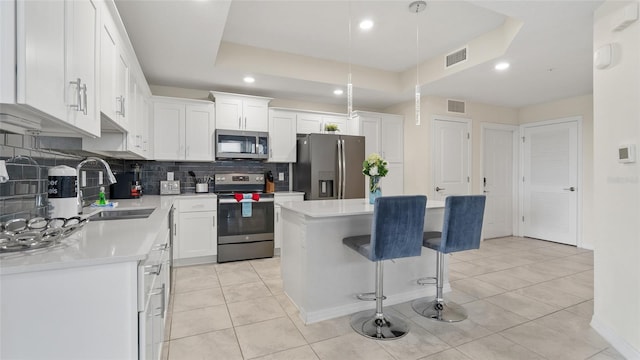 kitchen with decorative backsplash, appliances with stainless steel finishes, a kitchen island, sink, and white cabinetry