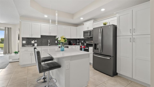 kitchen with a raised ceiling, a center island, white cabinets, and appliances with stainless steel finishes