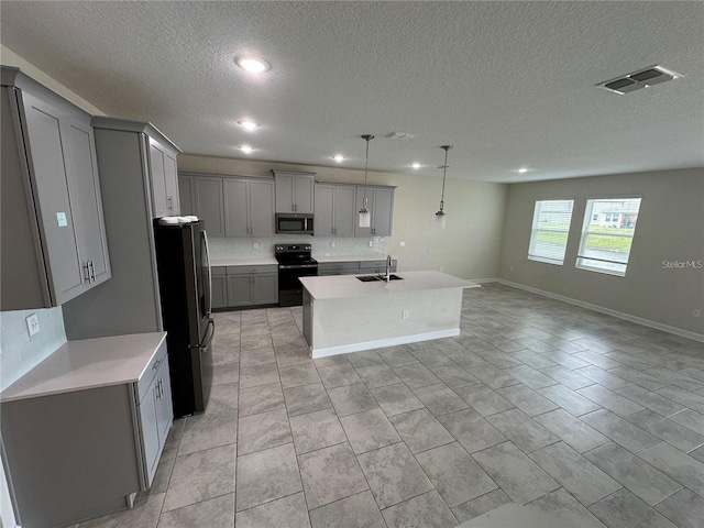 kitchen with pendant lighting, sink, a textured ceiling, appliances with stainless steel finishes, and an island with sink