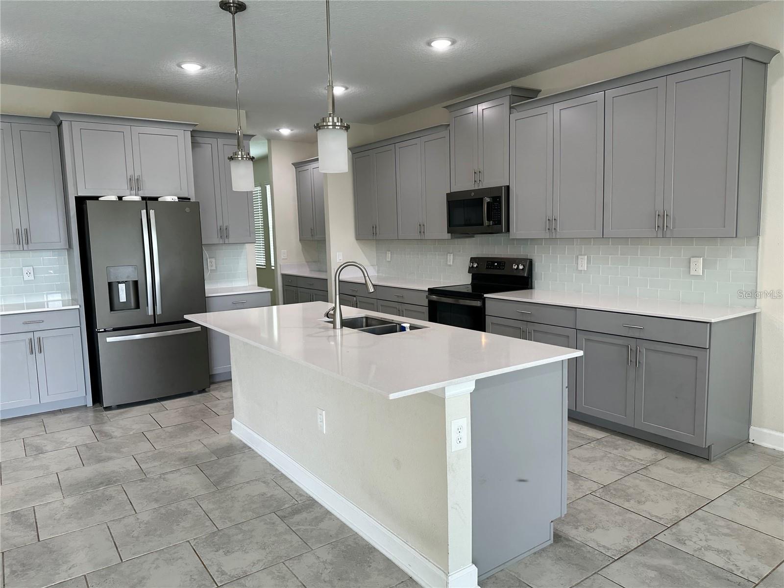 kitchen with gray cabinetry, sink, stainless steel appliances, an island with sink, and decorative backsplash