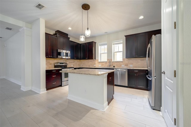 kitchen featuring light stone countertops, a center island, hanging light fixtures, decorative backsplash, and appliances with stainless steel finishes