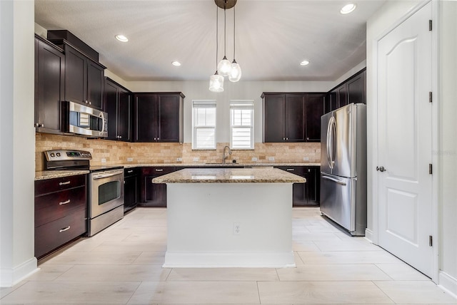 kitchen with light stone counters, stainless steel appliances, sink, decorative light fixtures, and a kitchen island