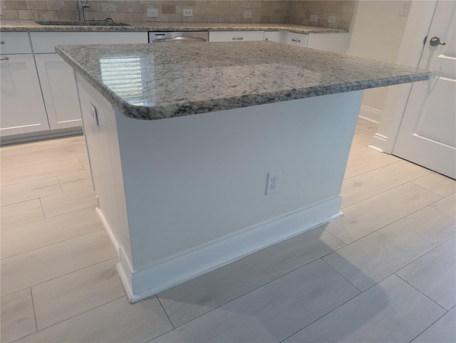 room details with a kitchen island, white cabinets, tasteful backsplash, light stone counters, and a sink
