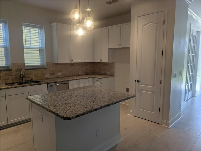 kitchen featuring stainless steel dishwasher, a sink, white cabinetry, and tasteful backsplash