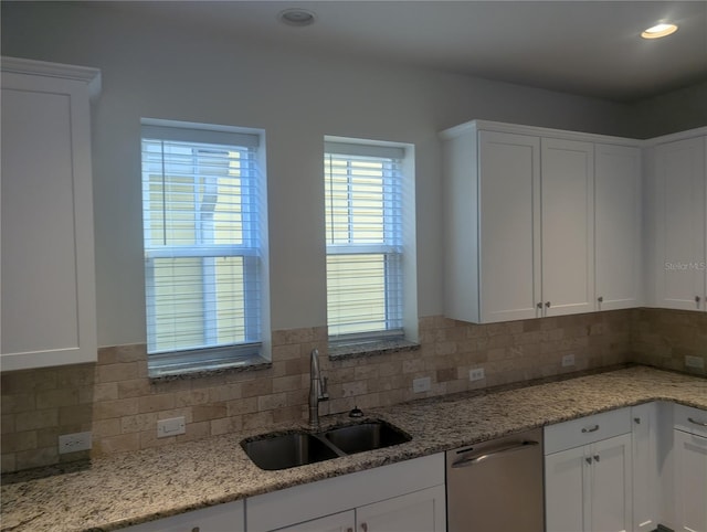 kitchen with a sink, white cabinets, stainless steel dishwasher, and backsplash