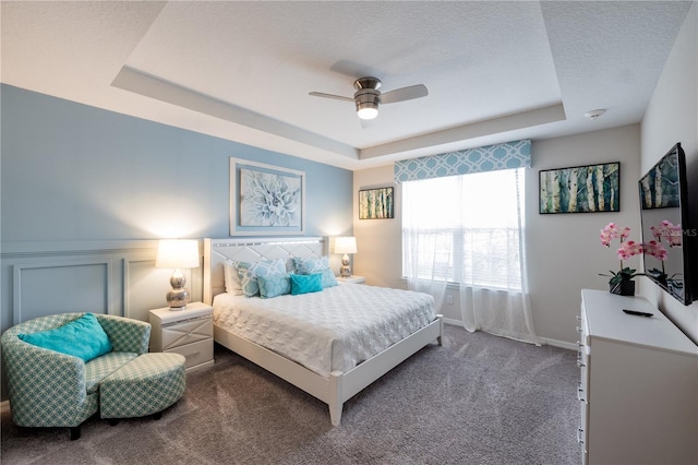 bedroom with a textured ceiling, ceiling fan, carpet flooring, and a raised ceiling