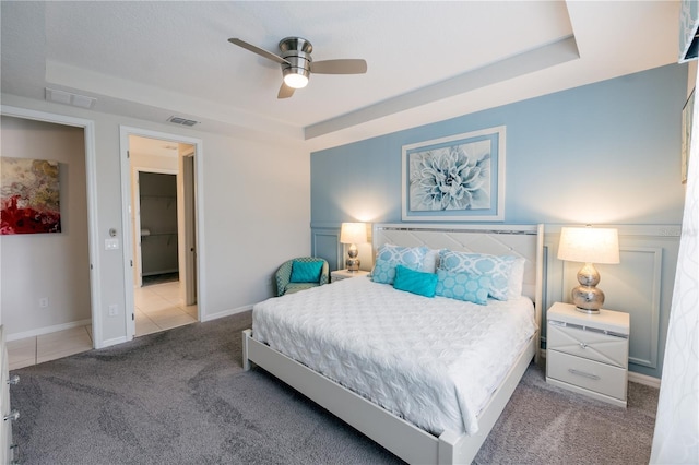 carpeted bedroom with ceiling fan and a tray ceiling