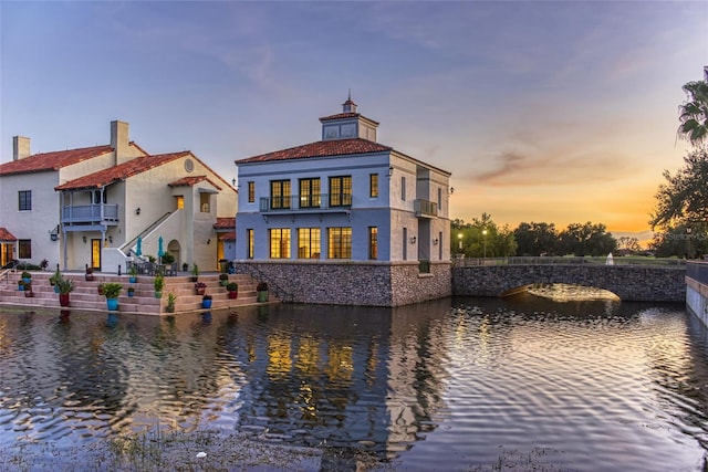 back house at dusk with cooling unit, a water view, and a balcony