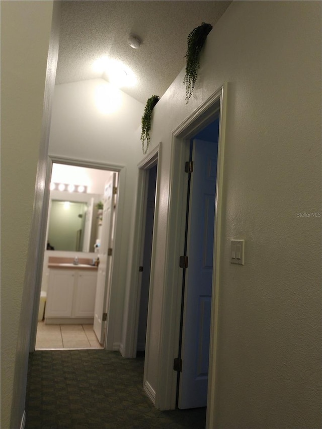 hall with tile patterned floors, a textured ceiling, and vaulted ceiling