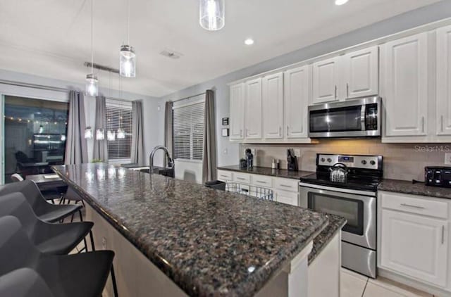 kitchen featuring stainless steel appliances, white cabinetry, hanging light fixtures, and a center island with sink