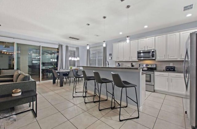 kitchen featuring appliances with stainless steel finishes, decorative light fixtures, white cabinets, a breakfast bar area, and light tile patterned flooring