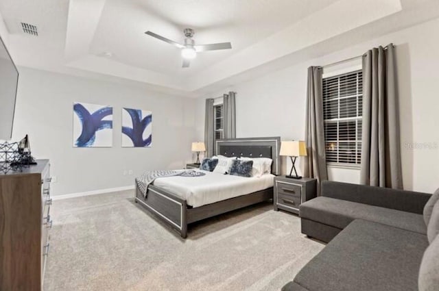 carpeted bedroom with a raised ceiling and ceiling fan