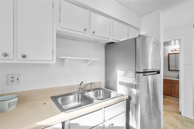 kitchen featuring stainless steel fridge, sink, white cabinets, and light tile patterned floors