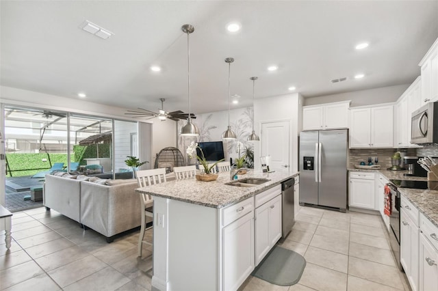 kitchen featuring ceiling fan, light stone countertops, an island with sink, a kitchen bar, and appliances with stainless steel finishes