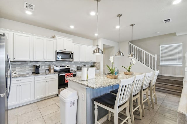 kitchen with a kitchen island with sink, white cabinets, hanging light fixtures, light stone countertops, and stainless steel appliances